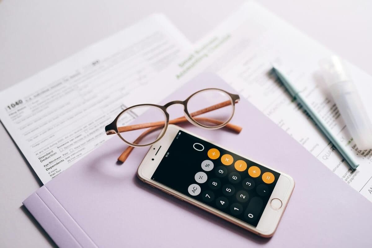 Calculator on a phone, glasses, pen, and tax forms on a light-colored surface