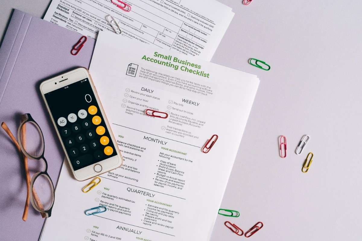 Small business accounting checklist, calculator, glasses, and paper clips on a desk